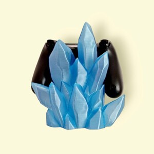 May include: A blue crystal-shaped video game controller holder. The holder is made of plastic and has a frosted finish. The controller is not included.