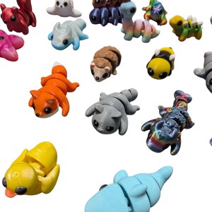 Peut inclure: Une collection de figurines d'animaux miniatures color&eacute;es. L'assortiment comprend un renard, un pingouin, une abeille et d'autres cr&eacute;atures dans diverses couleurs comme l'orange, le jaune et le bleu. Ces petites figurines d&eacute;taill&eacute;es sont probablement des jouets ou des objets d&eacute;coratifs.