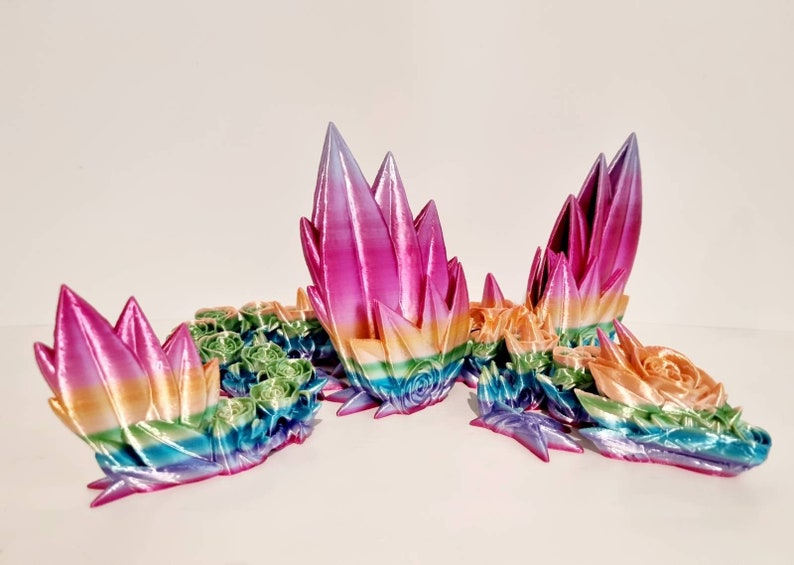 以下が含まれることがあります： 虹色の光沢のある色をした3Dプリントされたドラゴン彫刻。ドラゴンは頭、胴体、翼など、複数の部分で構成されています。ドラゴンは頭を上げた休息姿勢をとっています。