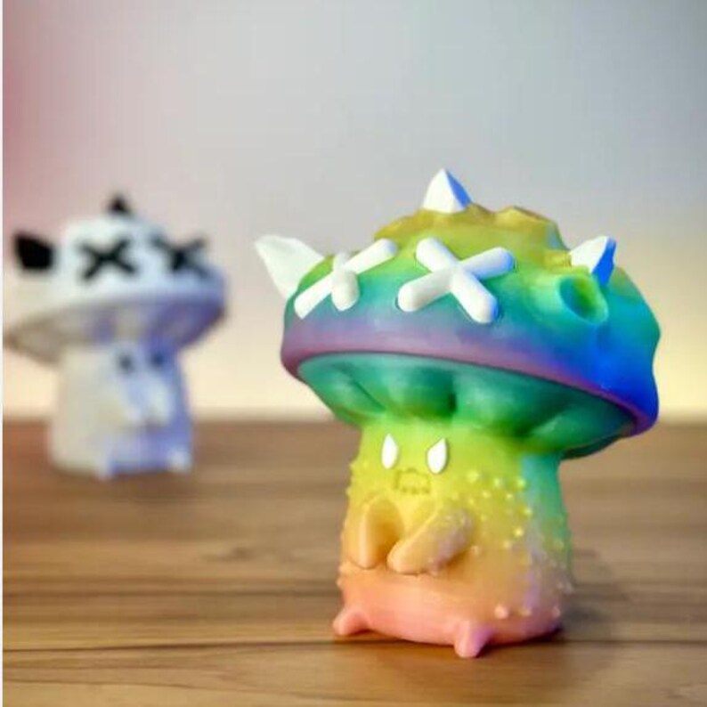May include: A rainbow-colored mushroom-shaped toy with a white X pattern on the top. The toy has a small, round body with a face and arms.