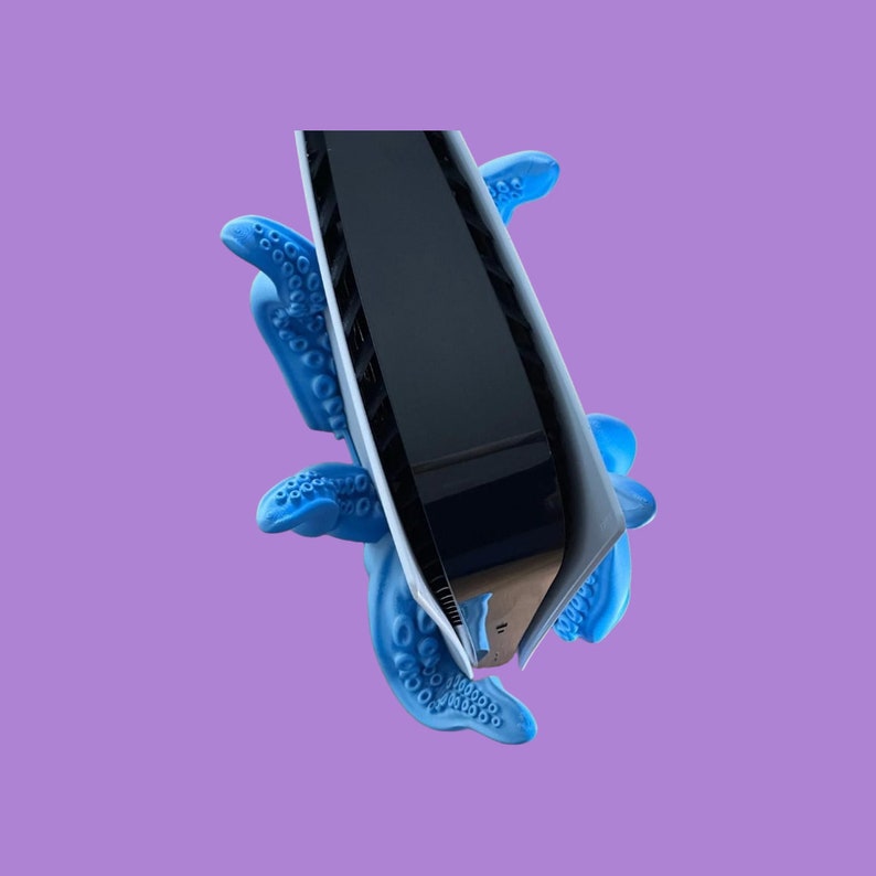 May include: A black rectangular object with a glossy finish is held by a blue rubber octopus-like hand. The object has a white edge and a slight curve.