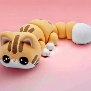May include: A small, orange and brown cat figurine with large eyes and a white tail. The figurine is made of a smooth, plastic-like material.