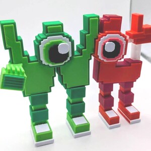 May include: Two pixelated figures, one green and one red, stand side-by-side. The green figure has a blocky arm and a large eye with white, black, and green details. The red figure has a similar design, with a raised arm. Both have blocky legs and feet.