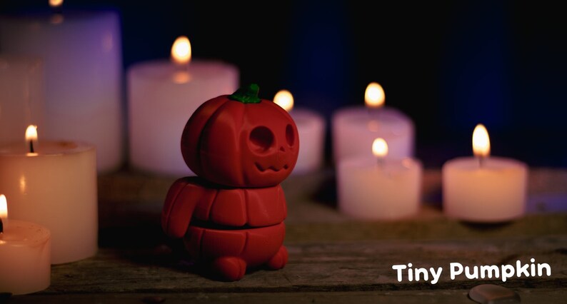 May include: A small, red, pumpkin-shaped figurine with a carved jack-o'-lantern face. The figurine is standing on a wooden surface in front of several lit candles.