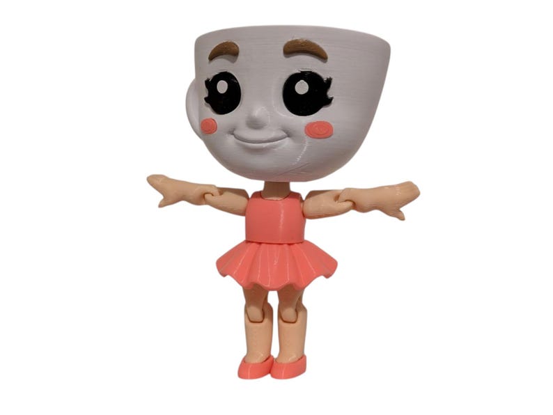 May include: A whimsical figurine of a teacup with a smiling face, rosy cheeks, and large black eyes. The teacup head is attached to a body wearing a pink dress and ballet shoes. The arms are outstretched.