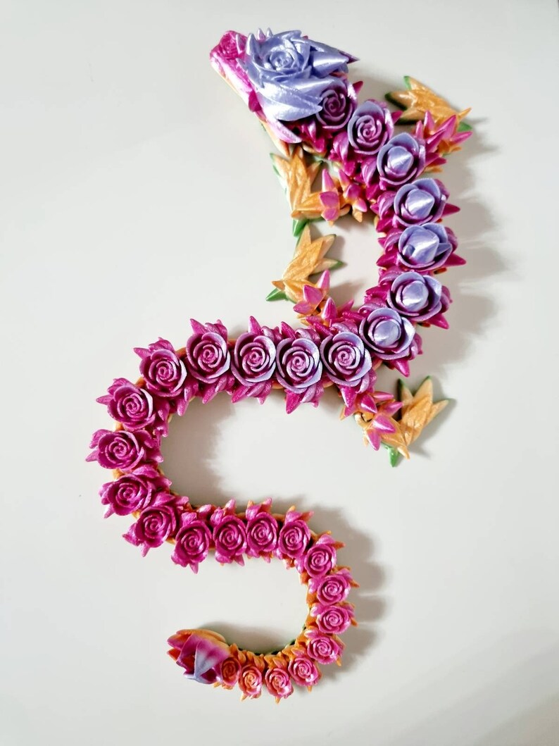 Peut inclure: Un dragon en tissu fait de roses, de couleur rose et violette. Le dragon est enroul&eacute; en forme de S, avec la t&ecirc;te en haut de l'image. Le dragon est compos&eacute; de nombreuses petites roses, et la queue est enroul&eacute;e.