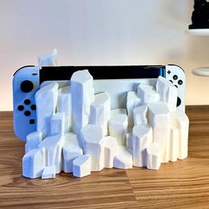 May include: White 3D printed stand shaped like a mountain range, designed to hold a Nintendo Switch console.