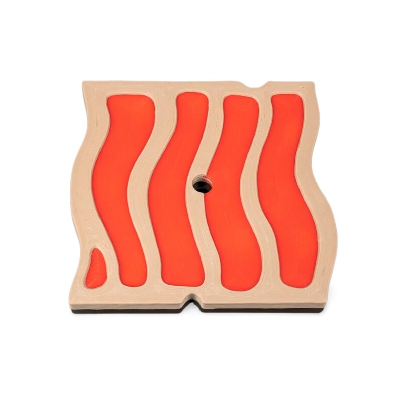 May include: A square, wooden coaster with a wavy design resembling bacon. The coaster features a light tan border with four vertical, wavy, orange stripes. A small, black hole is in the center. The bottom edge is black.