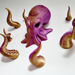 May include: A purple and gold octopus figurine with eight tentacles. The octopus is made of plastic and has a textured surface. The tentacles are separate pieces and can be attached to the octopus's body.