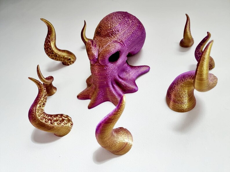 May include: A purple and gold octopus figurine with eight tentacles. The octopus is made of plastic and has a textured surface. The tentacles are separate pieces and can be attached to the octopus's body.