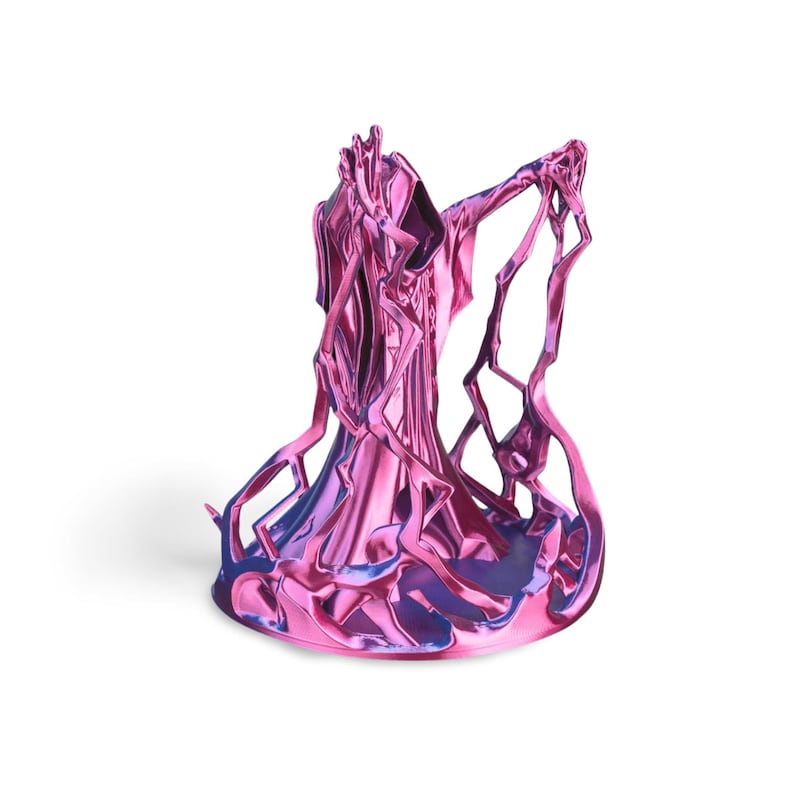 Puede incluir: Una escultura met&aacute;lica en tonos rosa y azul. La forma abstracta presenta una figura central con l&iacute;neas fluidas y extensiones intrincadas en forma de ramas. La escultura tiene un acabado brillante y se asienta sobre una base redonda.