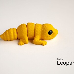 May include: A yellow plastic toy baby leopard gecko with black eyes. The toy is segmented and can be posed in different positions.