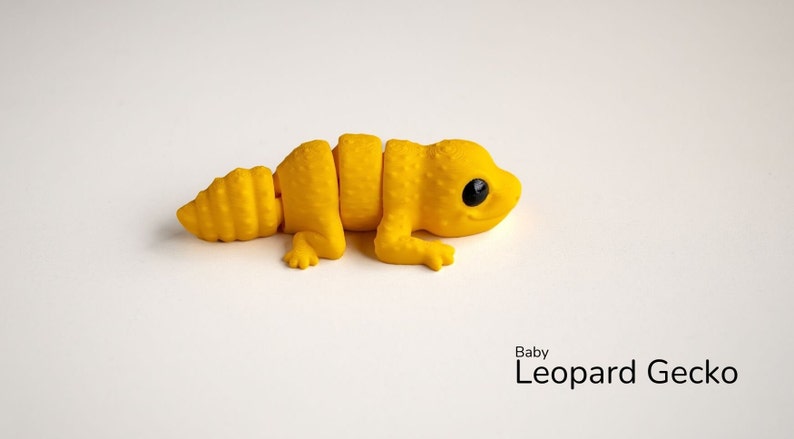May include: A yellow plastic toy baby leopard gecko with black eyes. The toy is segmented and can be posed in different positions.