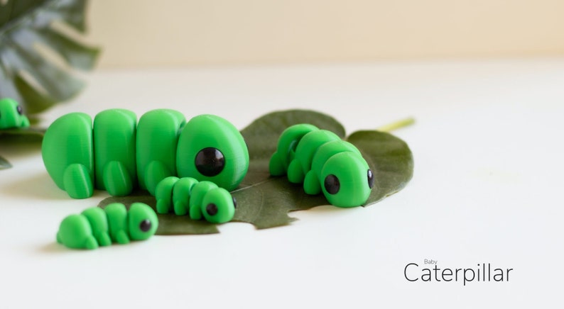 Puede incluir: Varias figuras de orugas verdes con ojos negros, colocadas sobre una hoja verde. Las figuras son de diferentes tama&ntilde;os, la m&aacute;s grande en el centro. El texto "Baby Caterpillar" es visible en la esquina inferior derecha.