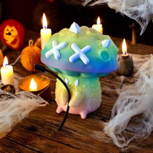 May include: A colorful, iridescent mushroom-shaped figurine with a white face and a black cord. The figurine is sitting on a wooden surface with candles and other decorations.