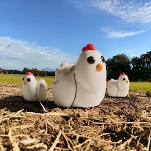 May include: Three white ceramic chicken figurines with red and orange accents. The chickens are arranged in a row on a brown surface with a green grassy background.
