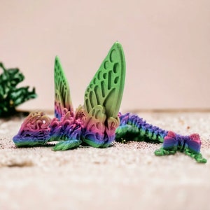 May include: A colourful, 3D printed dragon figurine with intricate details. The dragon is green, pink, and blue with a rainbow gradient effect. It has large wings and a long tail.