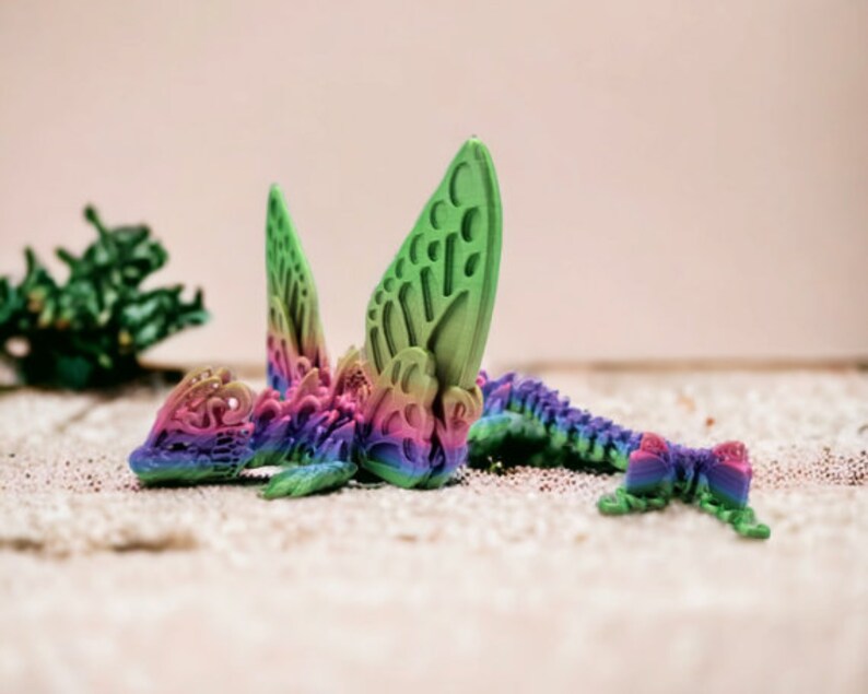May include: A colourful, 3D printed dragon figurine with intricate details. The dragon is green, pink, and blue with a rainbow gradient effect. It has large wings and a long tail.