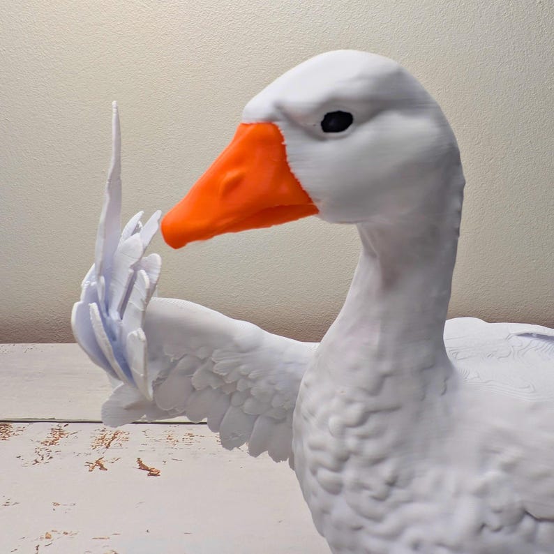 May include: A white goose sculpture with an orange beak and black eyes. The goose is holding up a wing, as if gesturing. The sculpture is detailed, with visible feather textures. The background is a neutral colour.