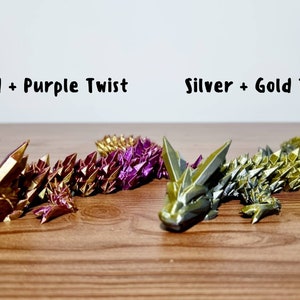 Peut inclure: Deux dragons en origami, l'un avec des &eacute;cailles dor&eacute;es et violettes, l'autre avec des &eacute;cailles argent&eacute;es et dor&eacute;es. Les dragons sont couch&eacute;s sur une surface en bois. Le texte "Gold + Purple Twist" est au-dessus du premier dragon, et le texte "Silver + Gold Twist" est au-dessus du deuxi&egrave;me dragon.