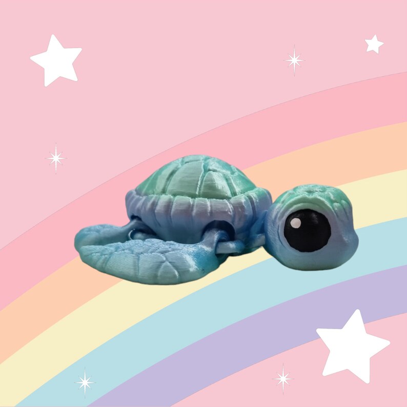 Puede incluir: Una peque&ntilde;a figura de tortuga marina impresa en 3D, de color azul y verde, con ojos grandes. La tortuga est&aacute; sentada sobre un fondo de arco&iacute;ris.