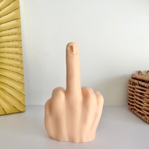 May include: A beige ceramic sculpture of a middle finger with a smiling face.