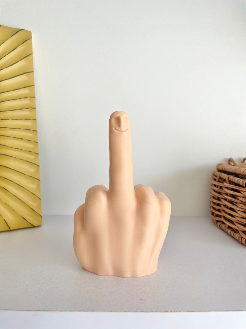 May include: A beige ceramic sculpture of a middle finger with a smiling face.