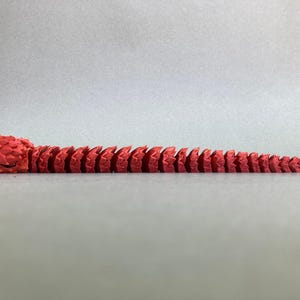 May include: A red segmented snake toy with a blue eye. The snake is made of plastic and is about 12 inches long.