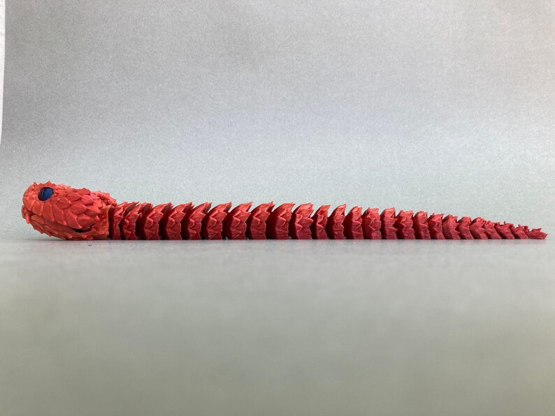 May include: A red segmented snake toy with a blue eye. The snake is made of plastic and is about 12 inches long.
