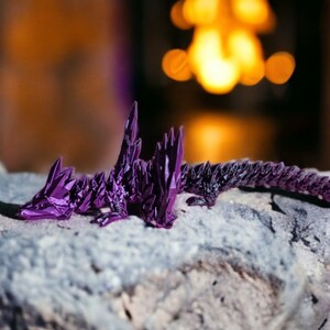 May include: A purple origami dragon with a detailed, spiky design, resting on a gray rock.