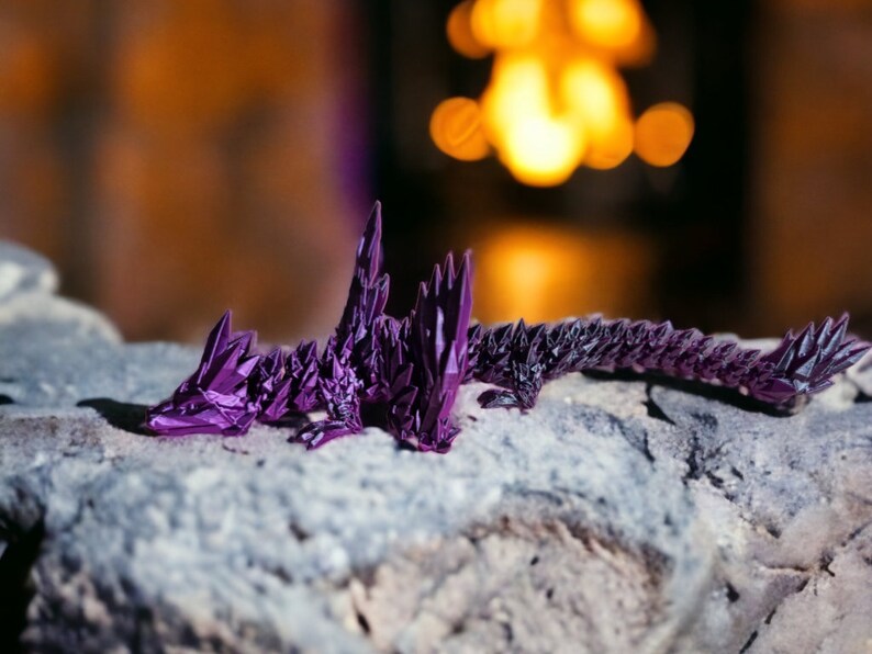 May include: A purple origami dragon with a detailed, spiky design, resting on a gray rock.