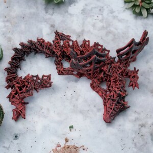 May include: A red and black decorative sculpture with an intricate, openwork design. The sculpture has a complex, organic shape, possibly resembling a dragon or abstract form. The colour palette is primarily red with black accents, creating a striking contrast.