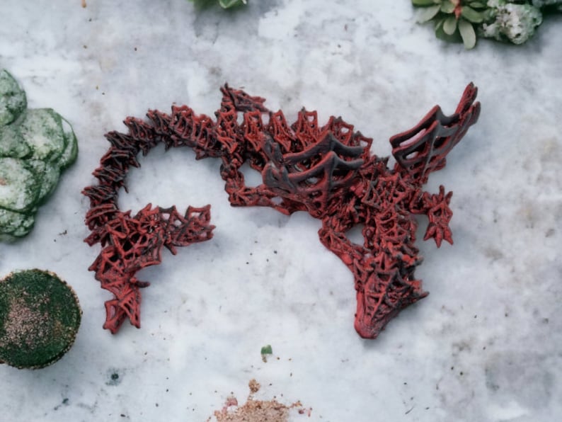 May include: A red and black decorative sculpture with an intricate, openwork design. The sculpture has a complex, organic shape, possibly resembling a dragon or abstract form. The colour palette is primarily red with black accents, creating a striking contrast.