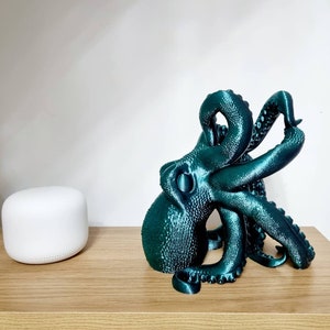 May include: A teal blue 3D printed octopus sculpture with a textured surface. The octopus is curled up with its tentacles reaching out.