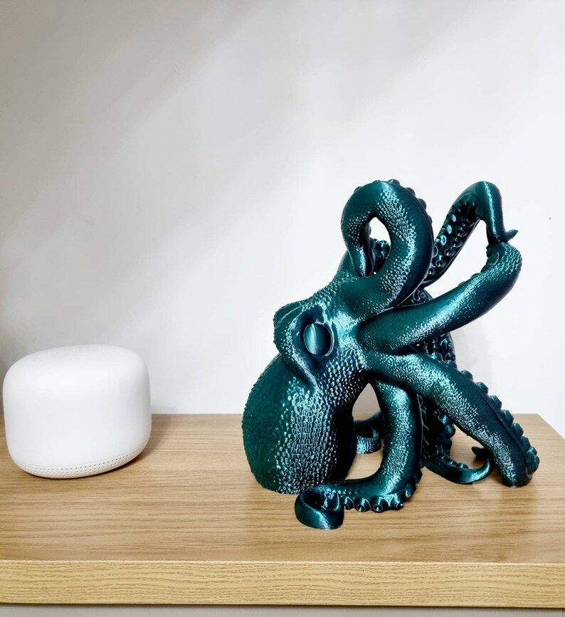 May include: A teal blue 3D printed octopus sculpture with a textured surface. The octopus is curled up with its tentacles reaching out.