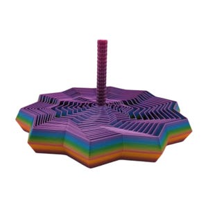 May include: A 3D-printed, multi-layered, star-shaped object with a central, cylindrical post. The base transitions from orange to purple, with a rainbow gradient. The post is a deep magenta color. The object is designed with a geometric pattern.