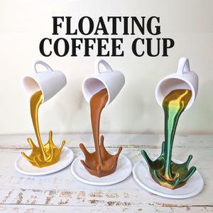 Puede incluir: Tres tazas de café blancas con asas, cada una aparentemente vertiendo un líquido de diferente color: dorado, marrón y verde. El líquido forma un chapoteo sobre un platillo blanco. El texto "FLOATING COFFEE CUP" está encima de las tazas.