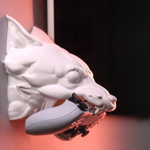 Puede incluir: Soporte de pared de cabeza de lobo de cer&aacute;mica blanca con un mando de videojuego blanco en su boca.