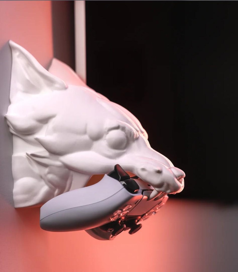 Puede incluir: Soporte de pared de cabeza de lobo de cer&aacute;mica blanca con un mando de videojuego blanco en su boca.