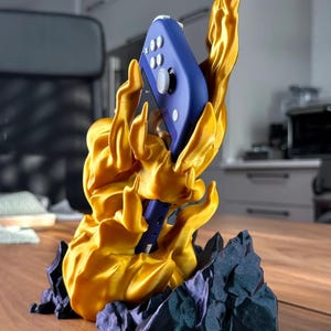 May include: A gold 3D printed stand shaped like a flame holding a blue Nintendo Switch controller.