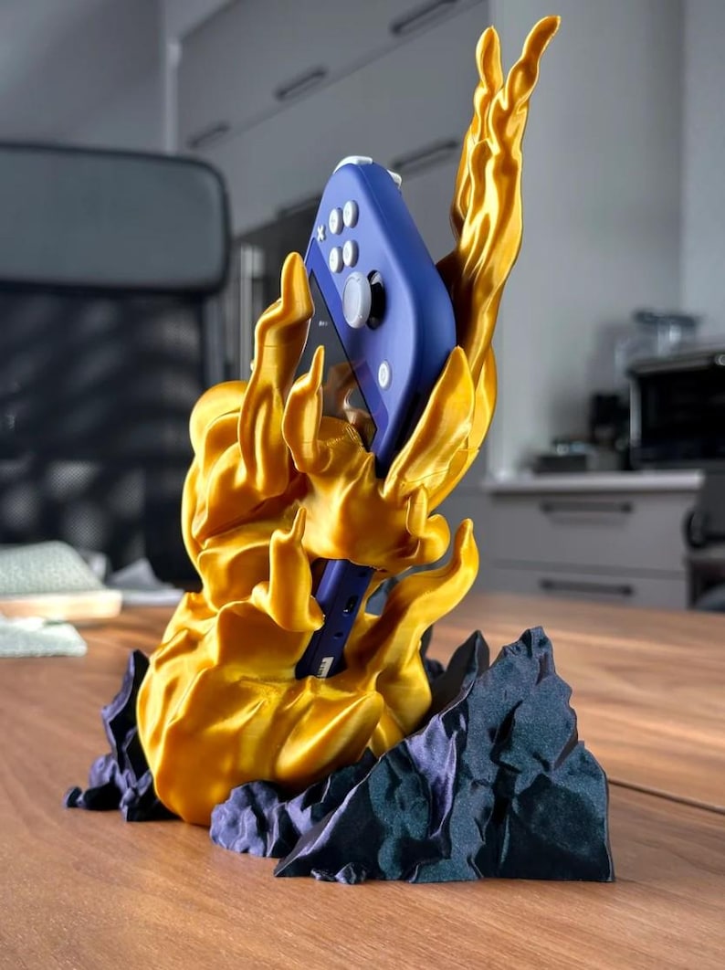 May include: A gold 3D printed stand shaped like a flame holding a blue Nintendo Switch controller.