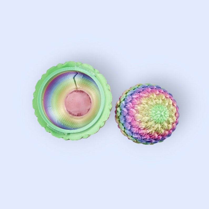 May include: A rainbow-colored, decorative egg with a matching lid. The lid is open, revealing the inside of the egg, which is also rainbow-colored.