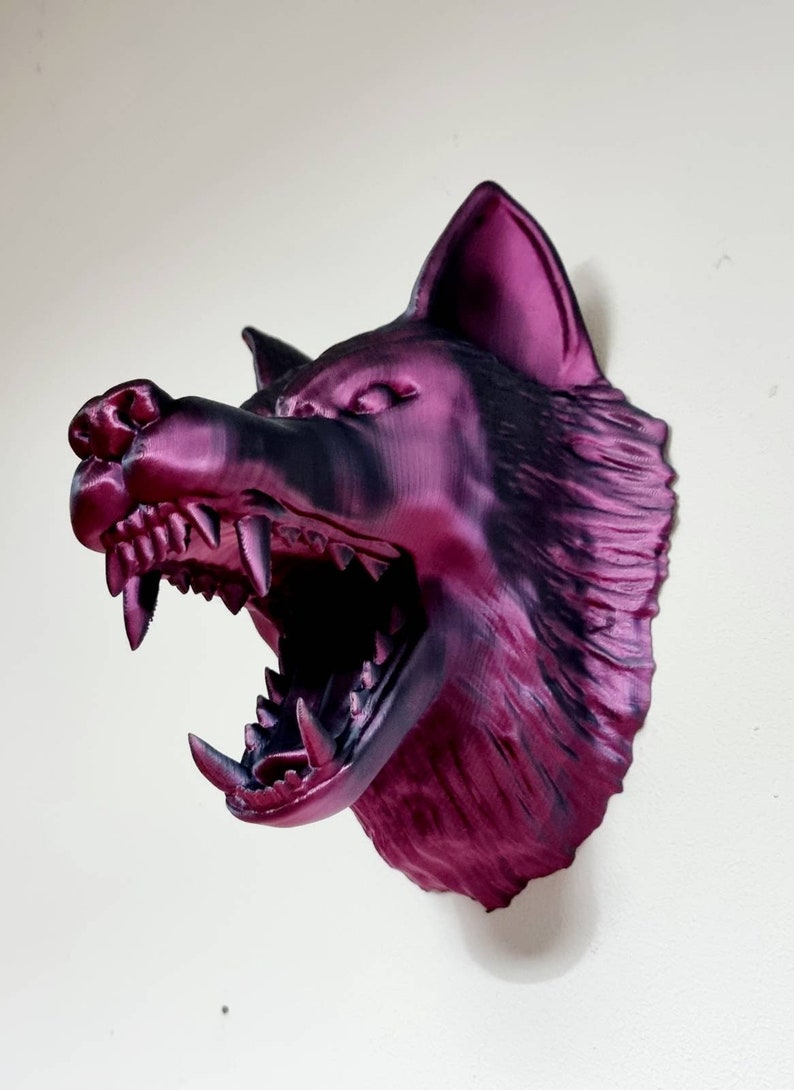 May include: A 3D-printed wolf head sculpture in shades of purple and black, mounted on a wall. The wolf's mouth is open, revealing sharp teeth. The sculpture is a decorative item.