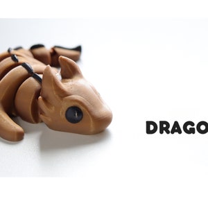 May include: A brown, articulated dragon figurine with black eyes. The figurine is lying on its side with its head turned to the right. The word "DRAGON" is printed in black letters on a white background.