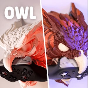 Puede incluir: Un soporte para mando de videojuegos con forma de búho esculpido en dos combinaciones de colores: blanco y rojo, y marrón y morado. La palabra "OWL" está impresa en letras blancas grandes encima del búho. El mando se sujeta en las garras del búho.
