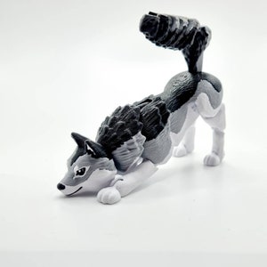 May include: A gray and white plastic toy wolf figurine in a crouching pose. The wolf has a black nose and black eyes.