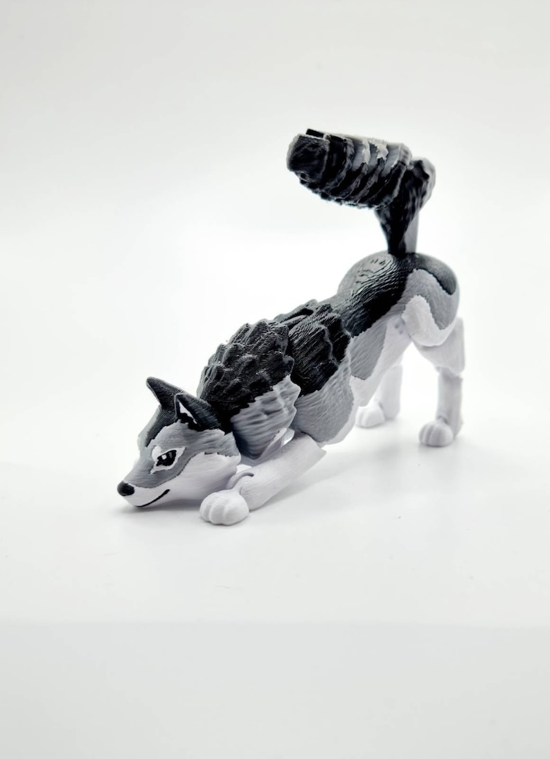 May include: A gray and white plastic toy wolf figurine in a crouching pose. The wolf has a black nose and black eyes.