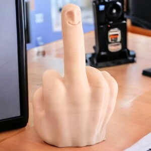 May include: A beige, 3D printed, middle finger sculpture with a smiling face on the index finger.