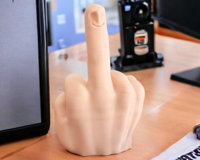 May include: A beige, 3D printed, middle finger sculpture with a smiling face on the index finger.