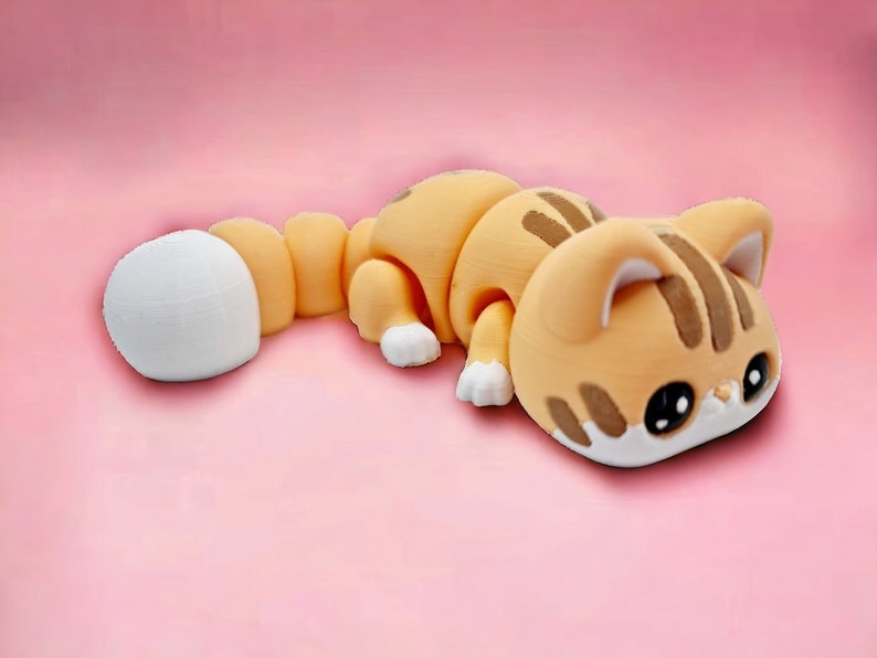 May include: A small, orange and white cat figurine with a segmented body. The cat is lying on its side with its head resting on the ground. The cat has black eyes and a white nose.